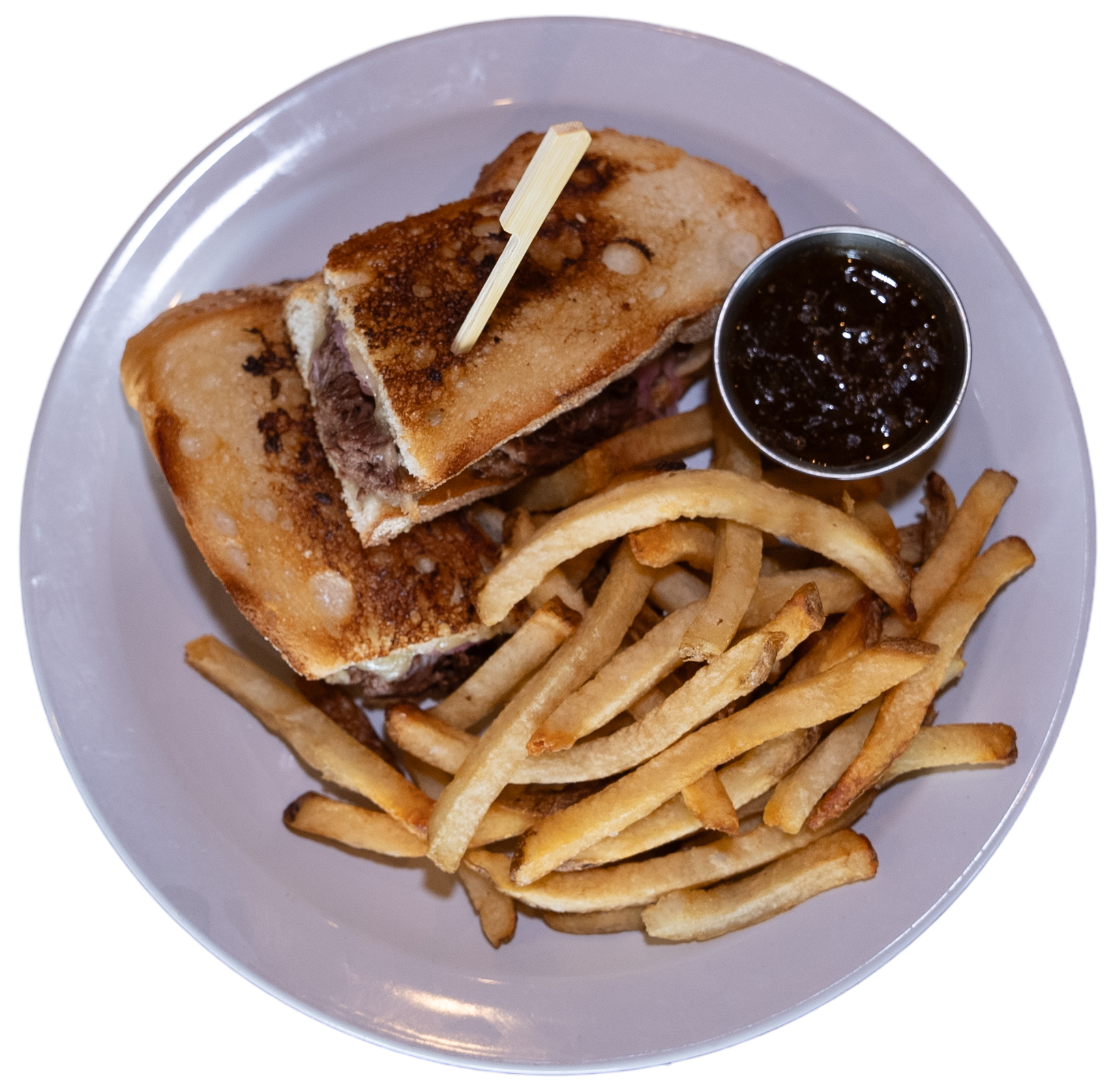 Plate with a sandwich cut in half, skewered with a toothpick, next to a portion of fries and a small container of dipping sauce.